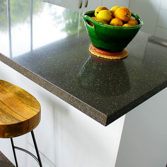 A white kitchen with Quartzforms Pebble Dark Grey quartz worktops, a chair, and a bowl of fruit