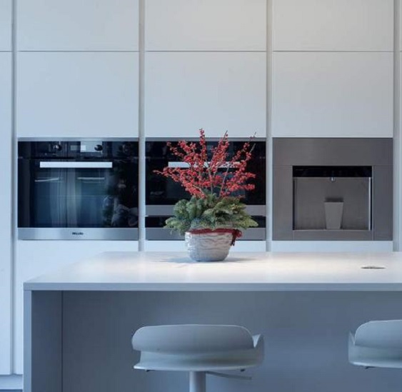 a white kitchen with an island in Quartzforms Cloudy White quartz and black appliances on the wall