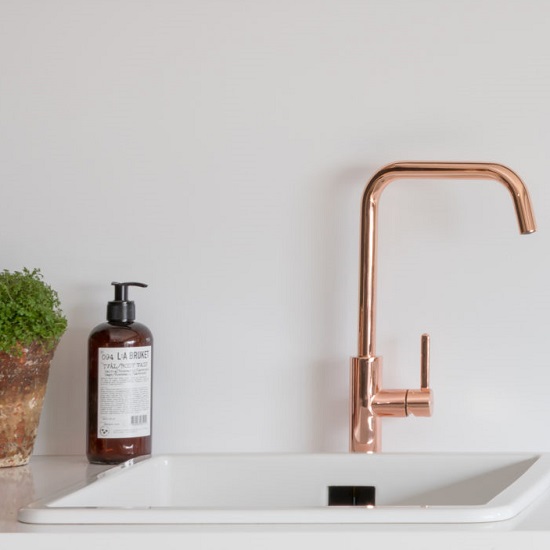 a kitchen worktop made from CRL Quartz Ice, a bronze coloured tap, a soap bottle and a plant