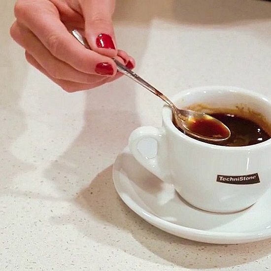 a close-up photo of Technistone Elegance Eco Nev worktops and a hand stirring a spoon on a cup of coffee