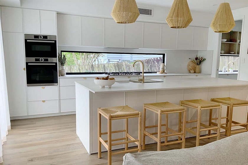 A photo of a coastal kitchen featuring Caesarstone Cloudburst worktops, white cabinets and wicker pendant lights
