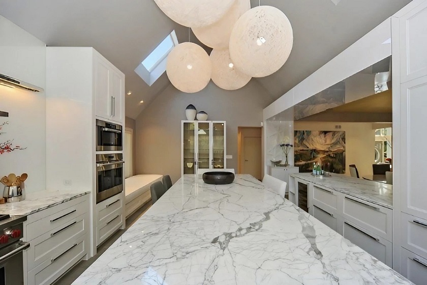 A contemporary kitchen with a Statuarietto marble island and worktops, and five round lamps in the ceiling