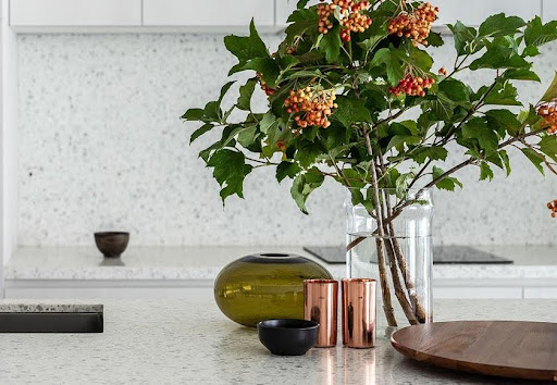 A plant in a vase on a white terrazzo worktop and matching backsplash behind