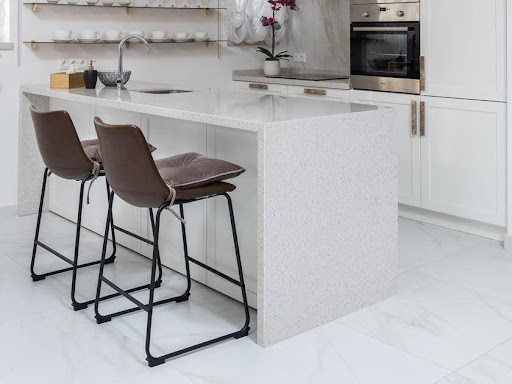A kitchen with a white terrazzo island and chairs