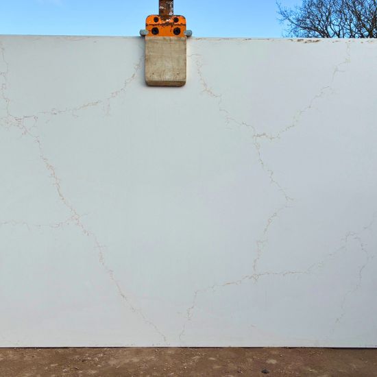 Giant slab of Calacatta Amber quartz in pristine white with delicate amber gold veins, being lifted by clamp in outdoor setting from the giant quartz collection