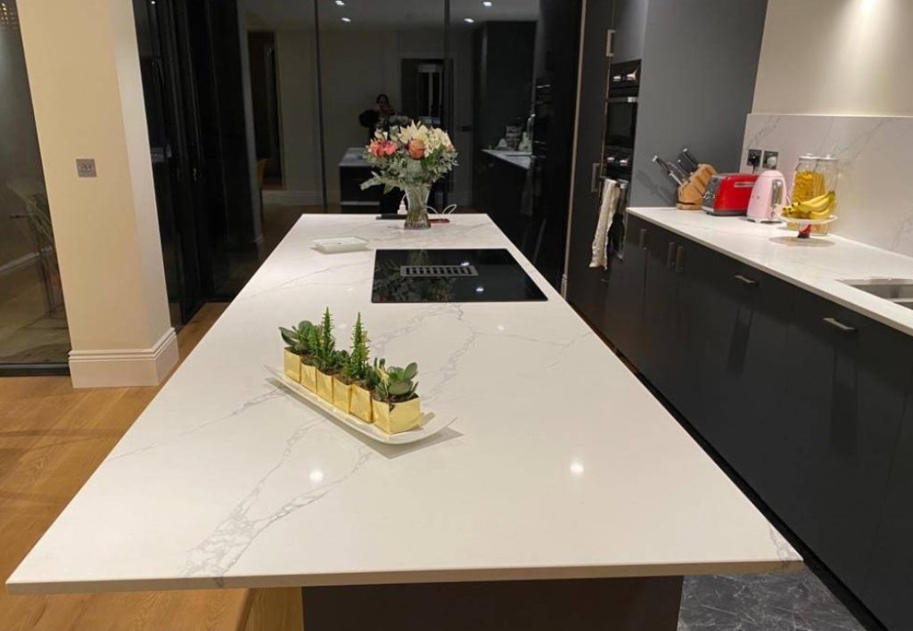 Polished white quartz kitchen island with black hob, succulents, and flowers in West Hampstead installation by Worktop Library