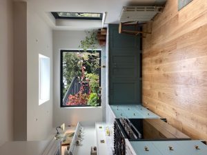 L-shaped Carrara marble kitchen with green cabinets, gas stove, gold tap, and garden window view in Shepherd's Bush London by Worktop Library
