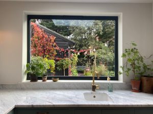 Carrara marble sink area with gold tap and potted plants overlooking garden in Shepherd's Bush installation by Worktop Library
