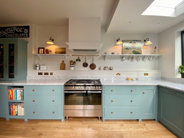 Polished Carrara marble worktops with green cabinets, stainless stove, and wall lights in Shepherd's Bush kitchen by Worktop Library