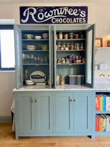 Open green pantry cabinet with Carrara marble top, stocked shelves, and books in London kitchen by Worktop Library