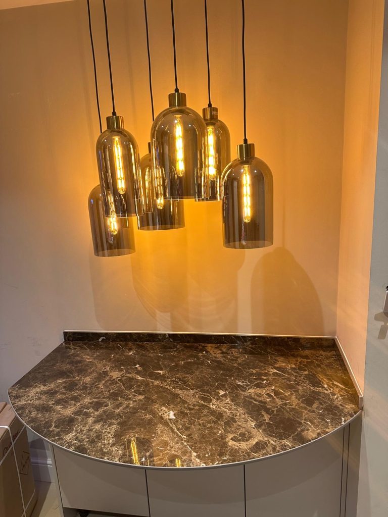Curved brown marble effect porcelain bar worktop with warm amber pendant lights in Banstead kitchen installation by Worktop Library