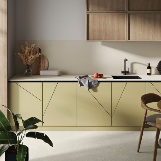 Neolith Creme kitchen worktop and splashback in warm cream, with yellow geometric cabinets, black sink, plants, and towel