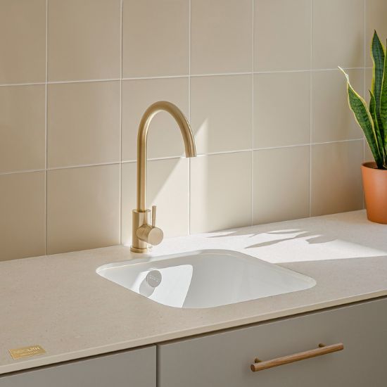 Neolith Creme kitchen sink worktop in cream tone with gold faucet, integrated white sink, and potted plant in bright space