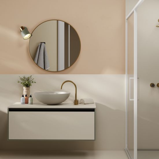 Neolith Creme bathroom vanity and walls in soft cream, with bowl sink, gold tap, round mirror, and shower in light-filled space