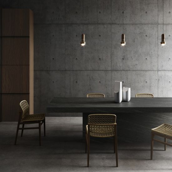 Neolith Ignea dining table in dark grey with wicker chairs, pendant lights, and vase in minimalist concrete room