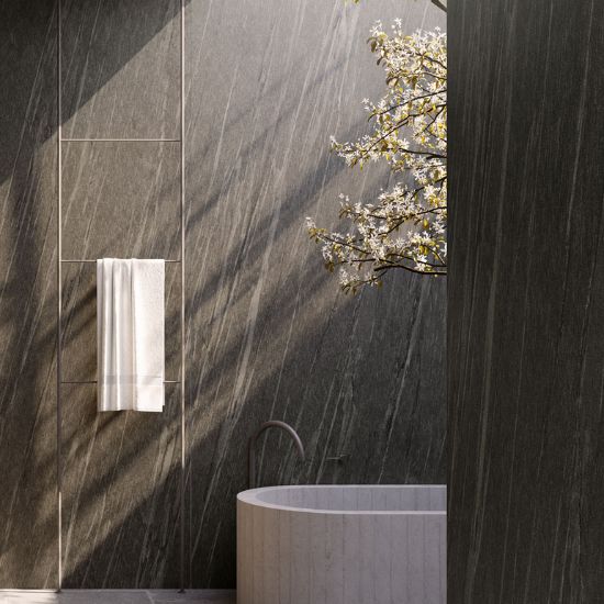 Neolith Ignea bathroom walls and tub in deep grey veining, with towel rail, blooming branch, and natural light