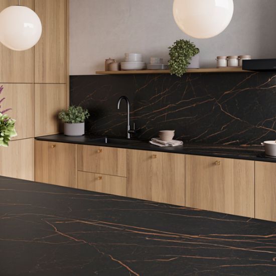 Neolith Mamba kitchen worktop and splashback in black gold-veined marble effect, wooden cabinets, plants, and pendant lights