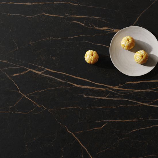 Close-up of Neolith Mamba sintered stone showing black background with golden veins, white plate, and mandarin oranges