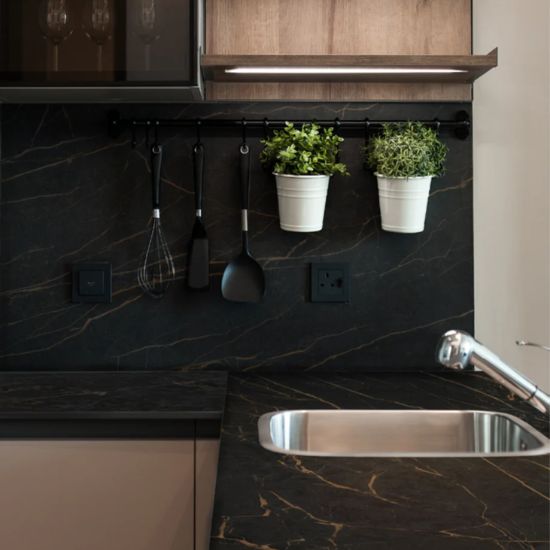 Neolith Mamba corner worktop with sink, hanging utensils, potted plants, and black gold veining in contemporary kitchen