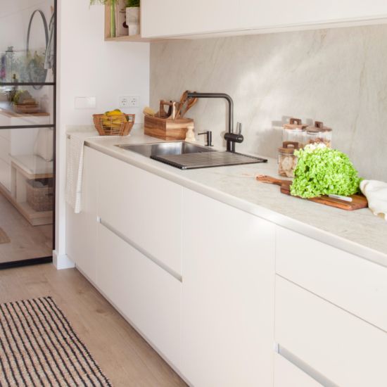 Neolith Taj Mahal kitchen worktop in creamy white veining with sink, black tap, wooden utensils, jars, and fresh greens in bright modern space