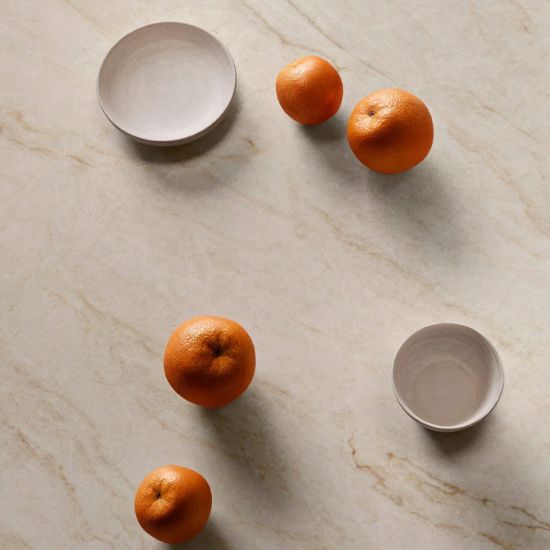Neolith Taj Mahal worktop close-up with scattered mandarins, white plate, and bowl on creamy veined surface