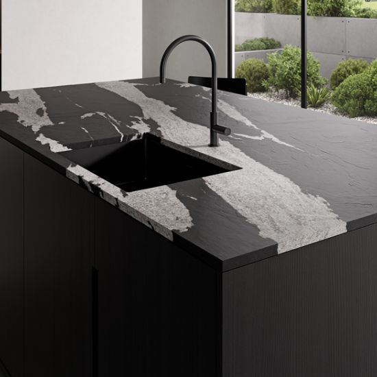 Neolith Victoria kitchen island in black with white veining, black sink and tap, against outdoor greenery in modern setting