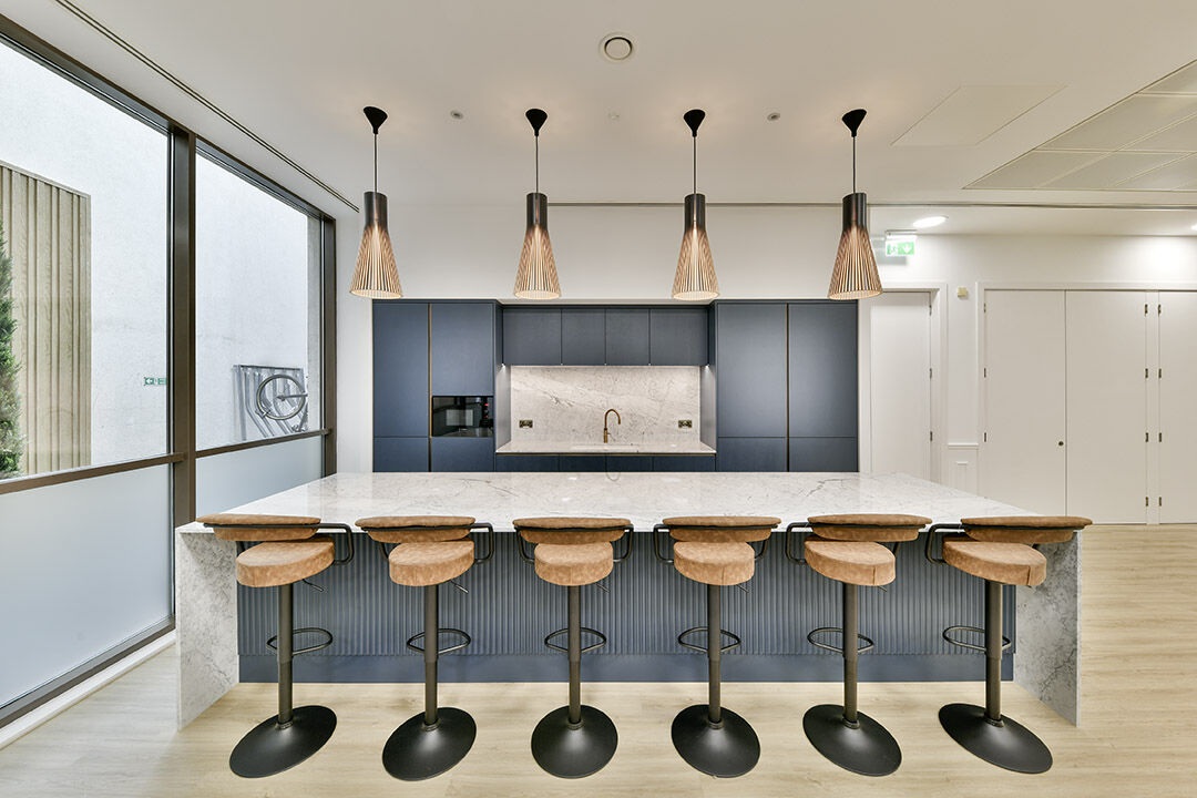 Front view of white marble worktop and bar stools in London office setup.