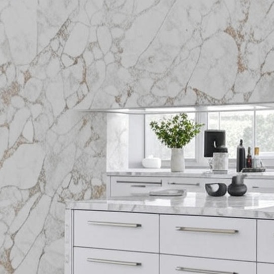 TextArabescato Oro quartz kitchen counters and backsplash in white with gold veins, including window view, green plant, bottles, and modern drawers in Essex Quartz Collection style