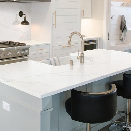 Calacatta Gold Giant Quartz kitchen island and worktops in brilliant white with grey and gold veins, featuring light grey cabinets, black leather bar stools, stainless steel range and bright modern kitchen