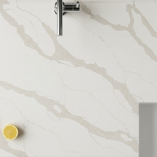 Calacatta Oro Giant Quartz kitchen worktop in bright white with soft grey veins, featuring chrome faucet, fresh lemon slice and basil leaf in a modern kitchen