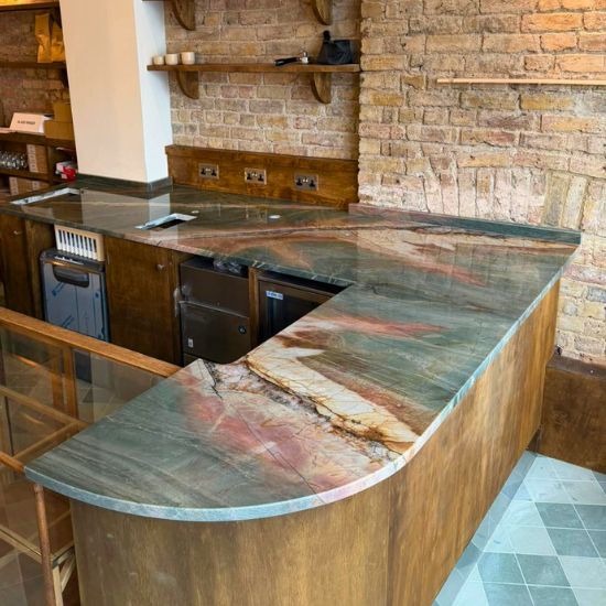 L-shaped Green Maestro Quartzite worktop with curved breakfast bar on wooden base in brick-walled bar