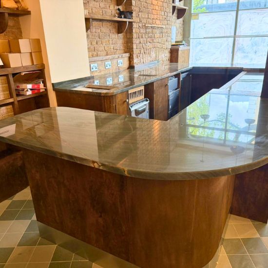 Curved wooden kitchen island with Green Maestro Quartzite worktop in showroom setting