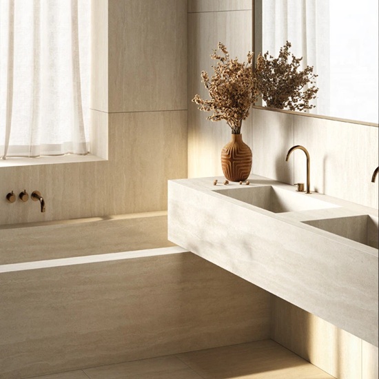 Sapienstone Travessa bathroom vanity and bathtub surround in soft beige travertine-effect with linear veining, featuring double sinks, brass fixtures and dried flowers in a serene modern bathroom