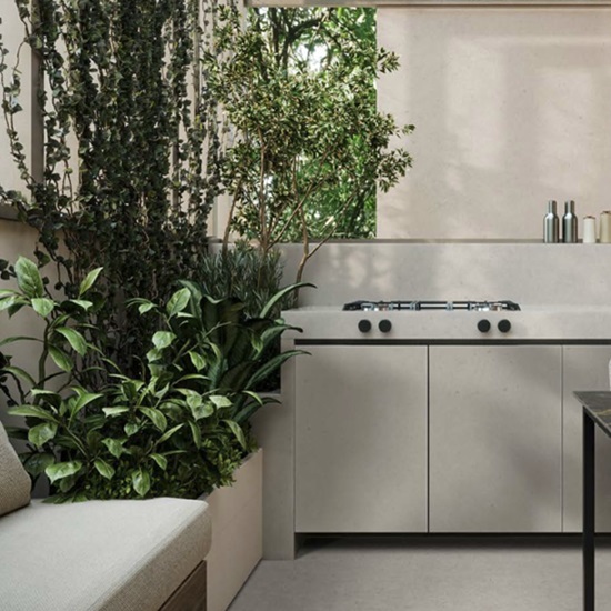 Techlam Limestone kitchen worktop and cabinetry in soft light grey with natural limestone texture, surrounded by lush green plants in a modern outdoor kitchen setting