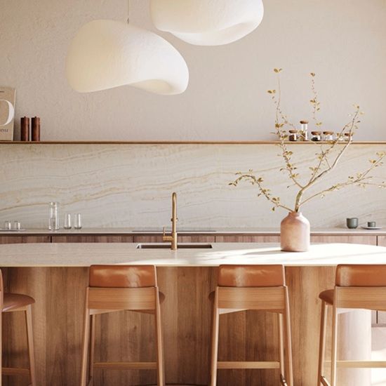 Modern kitchen with Caesarstone Onyxa installed as a full-height feature wall and splashback behind a wooden kitchen island, styled with organic pendant lights and warm neutral tones.