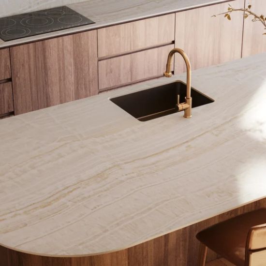 Curved kitchen island worktop in Caesarstone Onyxa with integrated sink, brass tap and warm timber cabinetry in a contemporary kitchen setting.